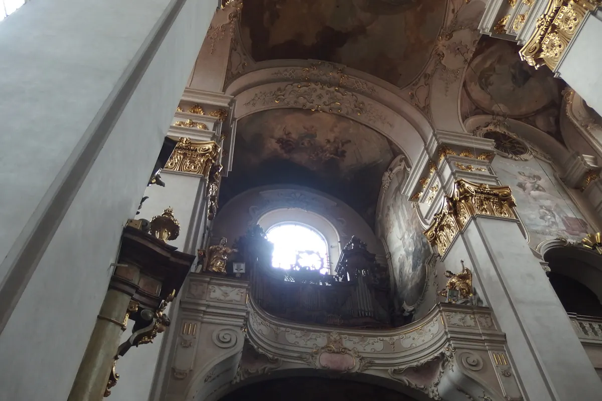 Looking up inside St Giles' Church at a curved gallery with a window behind it and gilded capitals on the pale pillars.